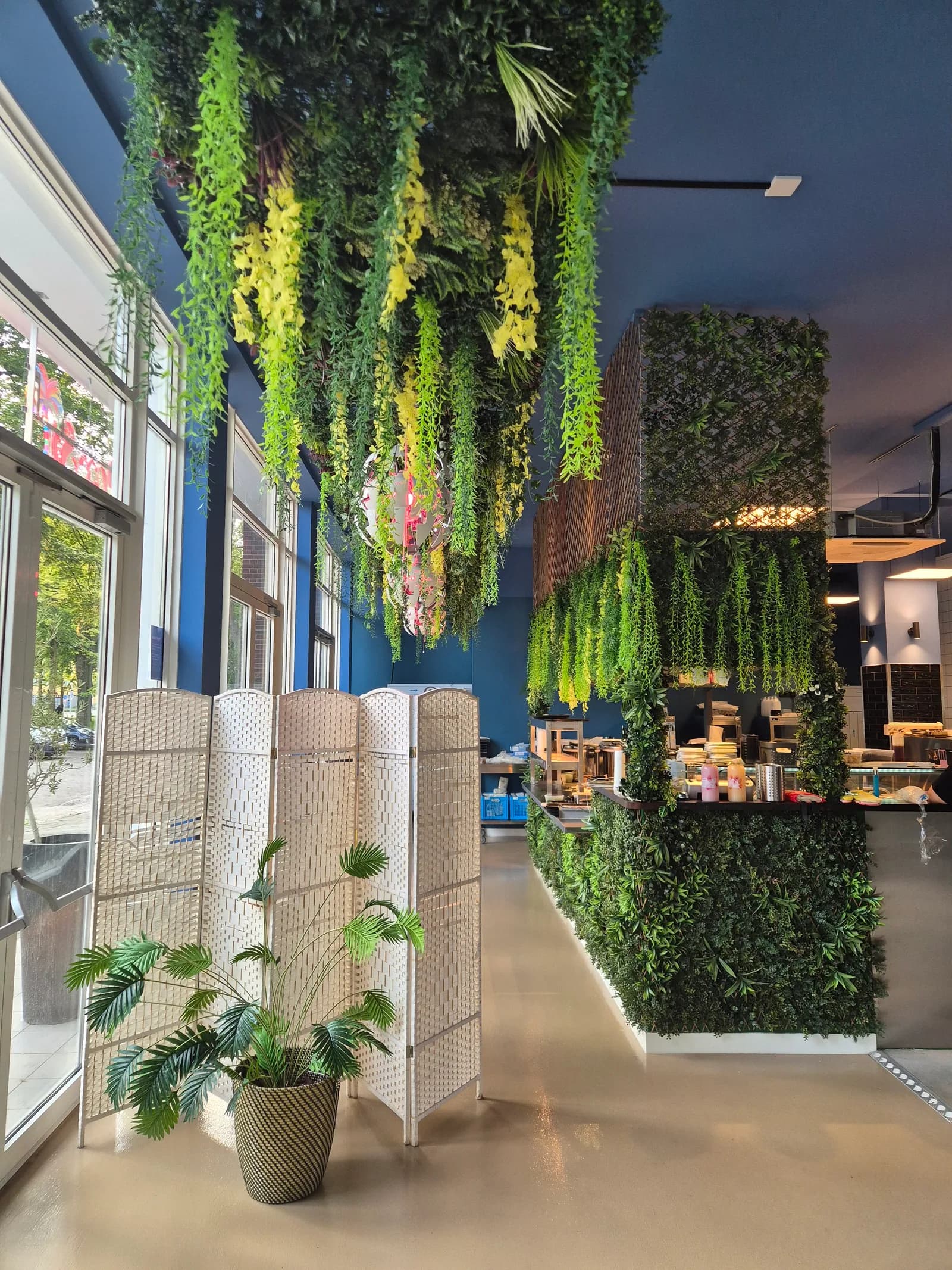 Plantenwand met hangende bloemen boven de open keuken en de vitrine