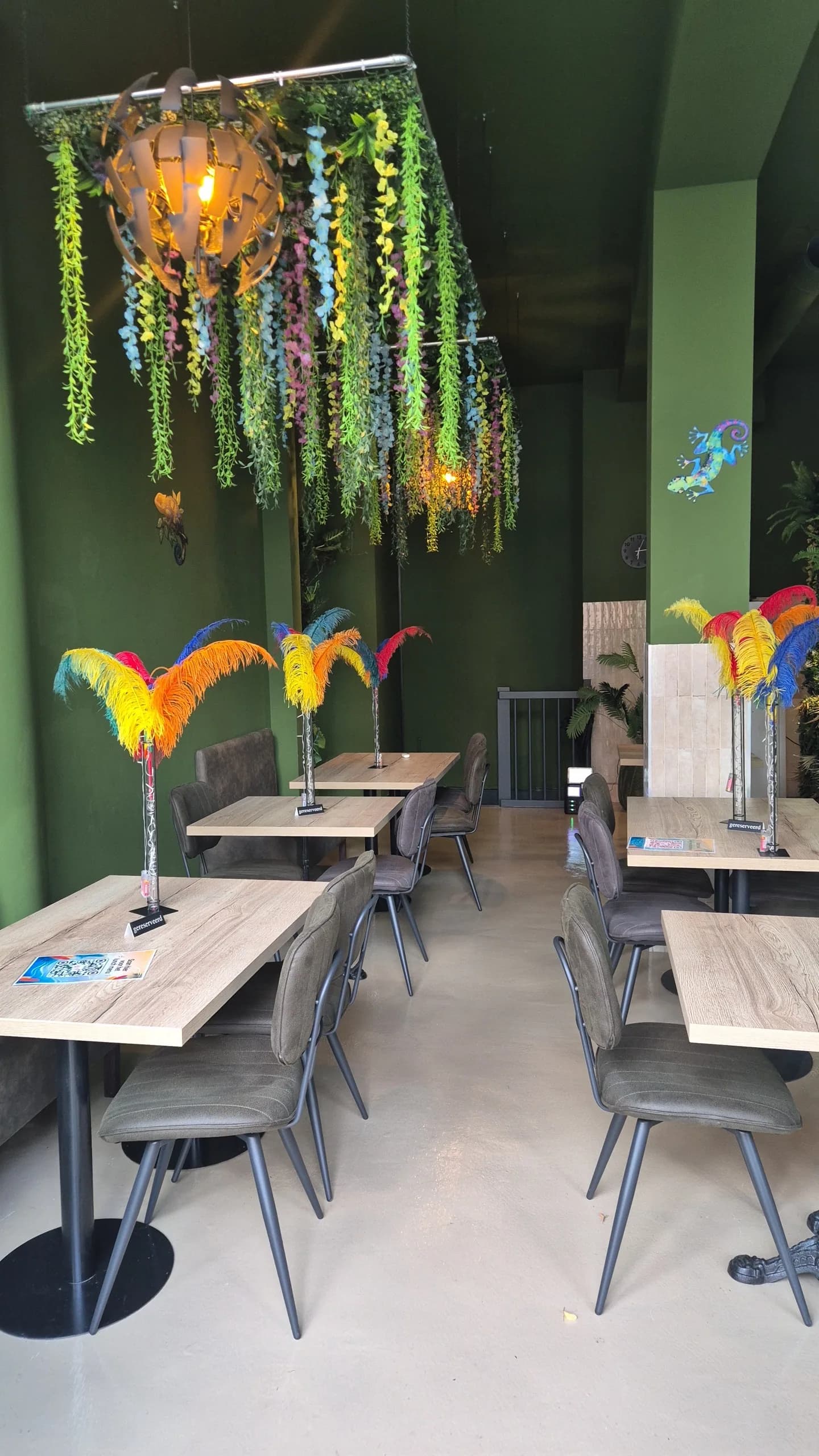 Zaal met groene wanden, houten tafels en gekleurde verendecoraties