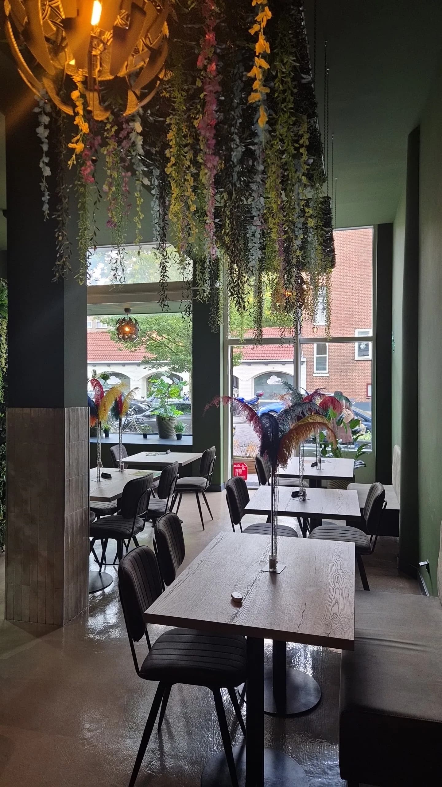 Tafels bij het raam met uitzicht op de straat en hangend groen aan het plafond