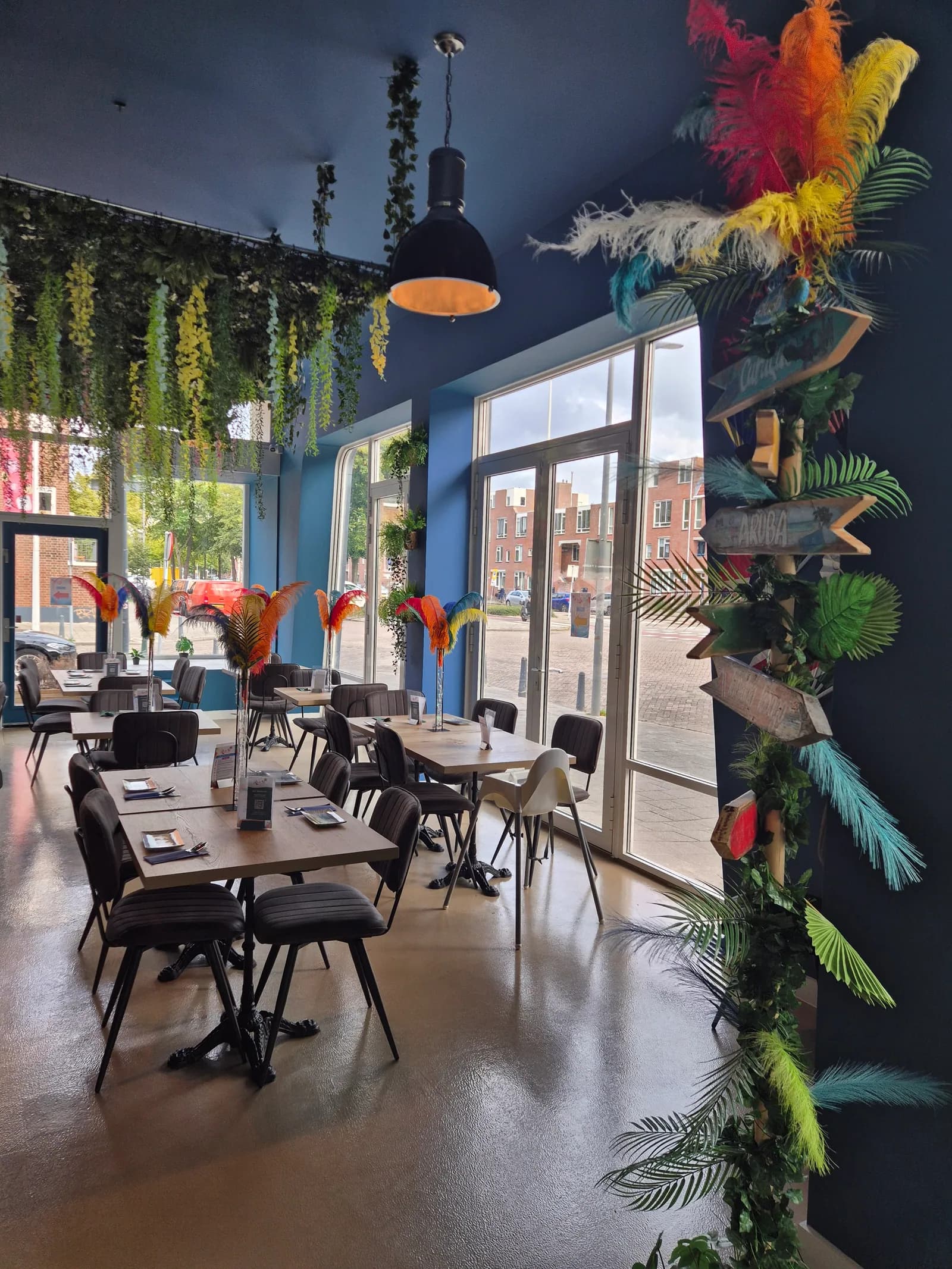 Zaal met hoge ramen, palmdecoratie en gekleurde veren op de tafels