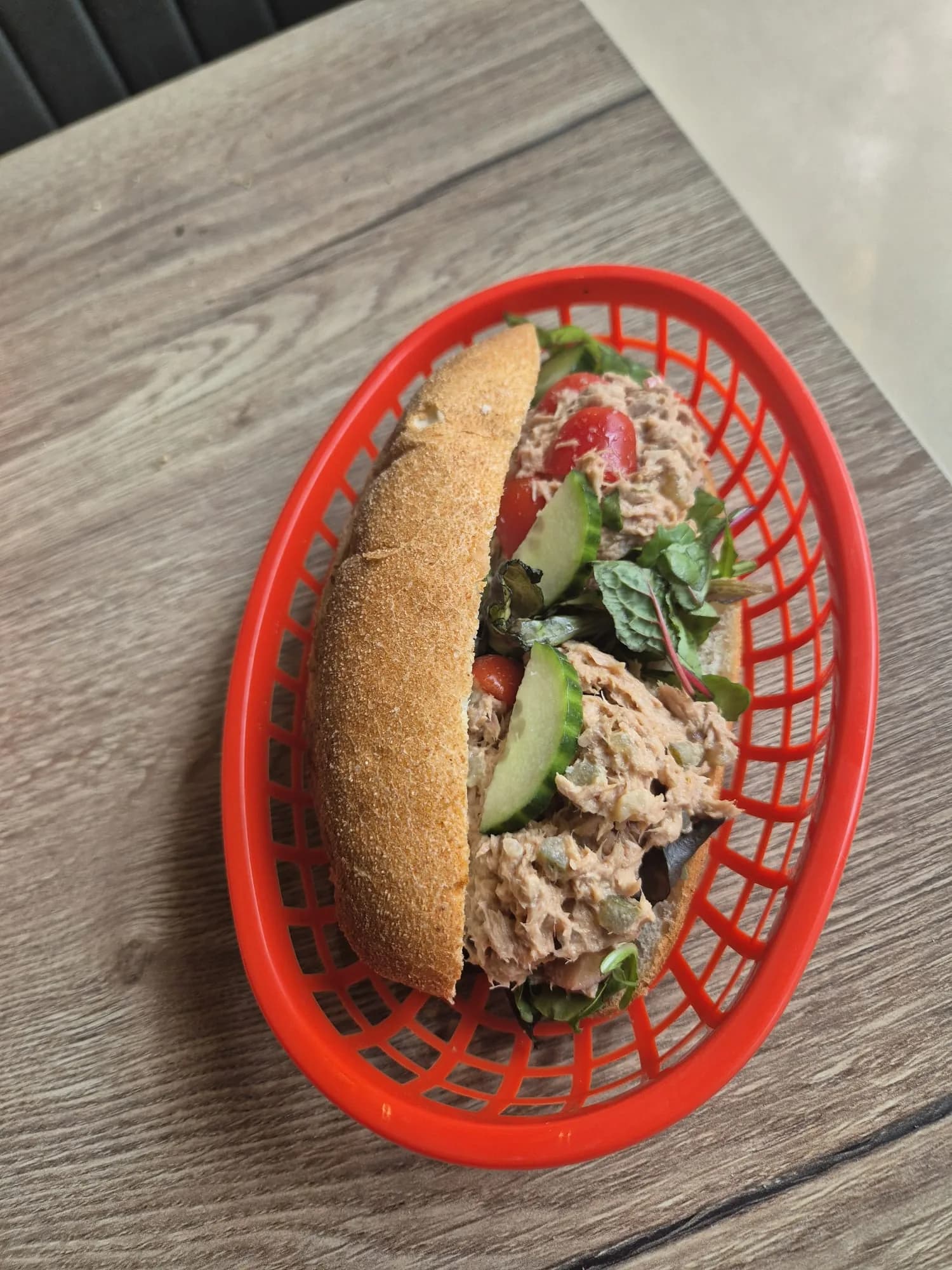 Belegd broodje met salade, tomaat en komkommer in een rood mandje